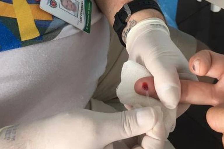 Profissional de saúde fura dedo de paciente e retira amostra de sangue