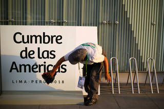 A woman cleans a banner ahead of the eighth Summit of the Americas in Lima