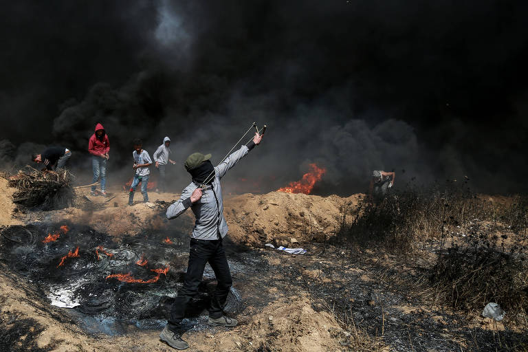Manifestante palestino usa estilingue para lançar pedras contra soldados israelenses durante conflito em Gaza
