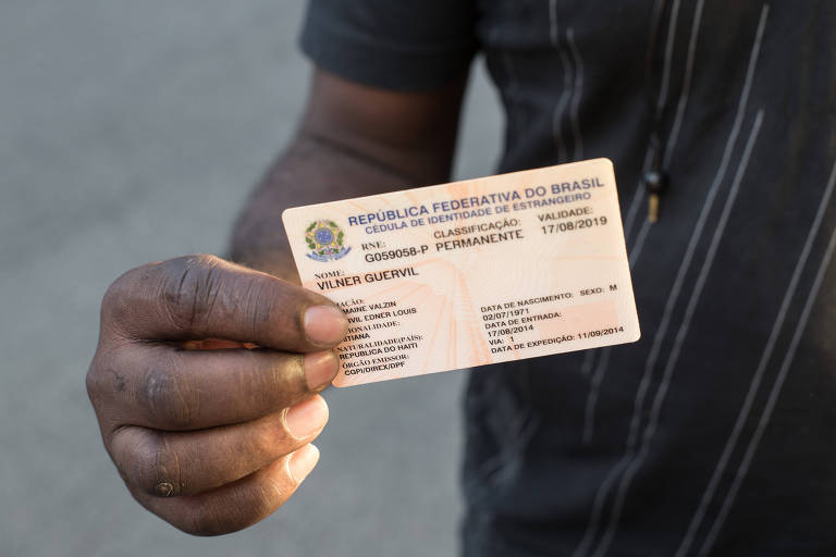 O imigrante haitiano Vilner Guervil, 44, mostra sua cédula de identidade de estrangeiro