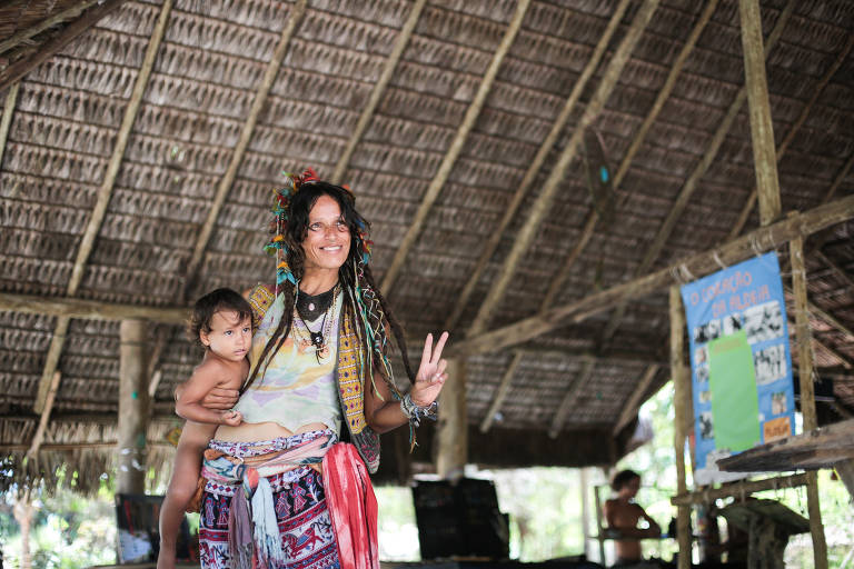 Hozana Silva, artesã e moradora da aldeia hippie de Arembepe, na Bahia, faz sinal de paz e amor enquanto segura a filha de um ano no colo