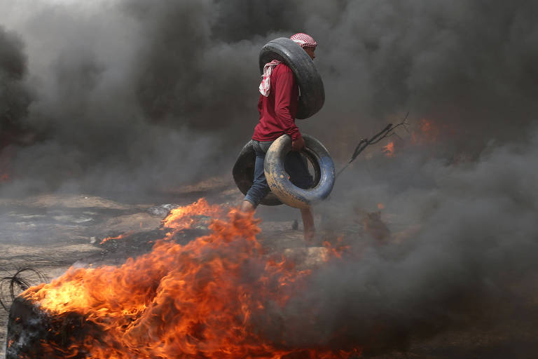 Manifestantes palestino carrega pneus durante o confronto com os militares israelenses 