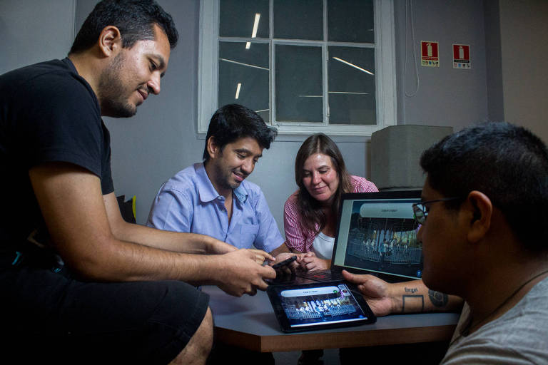 José Valencia, Carla Zeltcer, Antonio Ramos e Josué Arambide, da FazGame, em volta de uma mesa mexendo em seus aplicativos no computador, tablet e celular