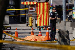 A police officer stands next to a victim of an incident where a van struck multiple people at a major intersection in Toronto's northern suburbs in Toronto