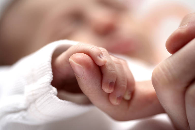 Imagem de um bebê recém-nascido segurando a mão da mãe