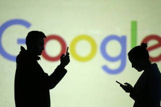 Silhouettes of mobile users are seen next to a screen projection of Google logo in this picture illustration