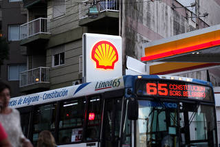 People walk as a bus passes a Shell gas station in Buenos Aires