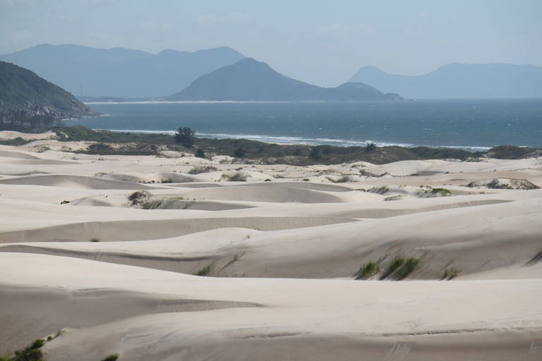 As dunas do Siriú aparecem em primeiro plano e são compostas por areia branca e fina. Ao fundo da foto, é possível ver o mar e a serra