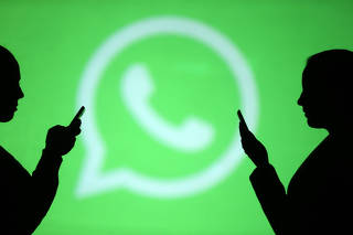 Silhouettes of mobile users are seen next to a screen projection of Whatsapp logo in this picture illustration