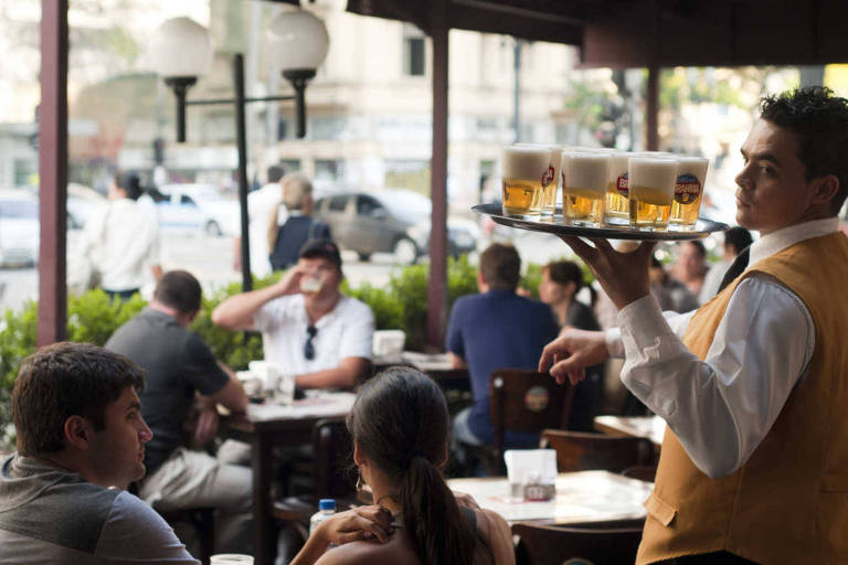 Garçom com bandeja cheia de copos com chopp em bar em São Paulo