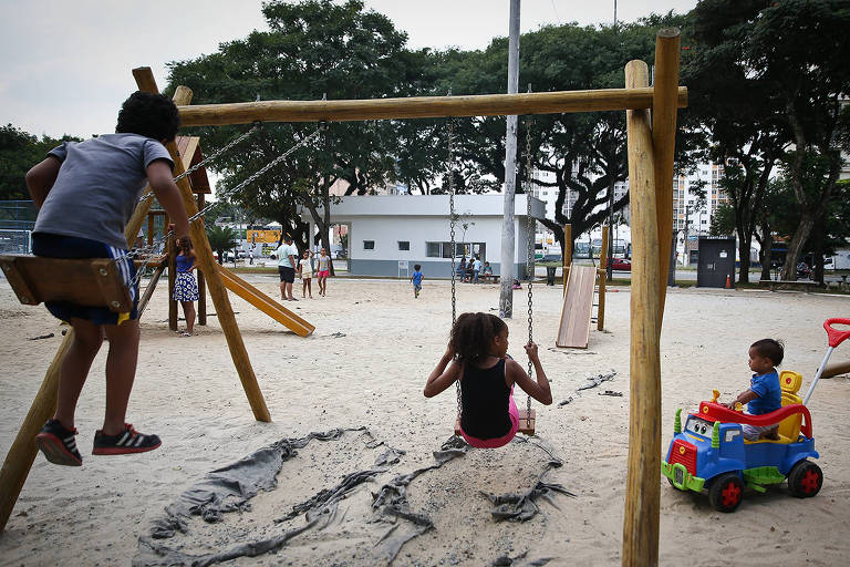 Crianças, em um parque de areia, brincam em um balanço