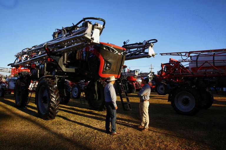 Imagem mostra duas pessoas próximas a máquinas agrícolas expostas numa feira agrícola