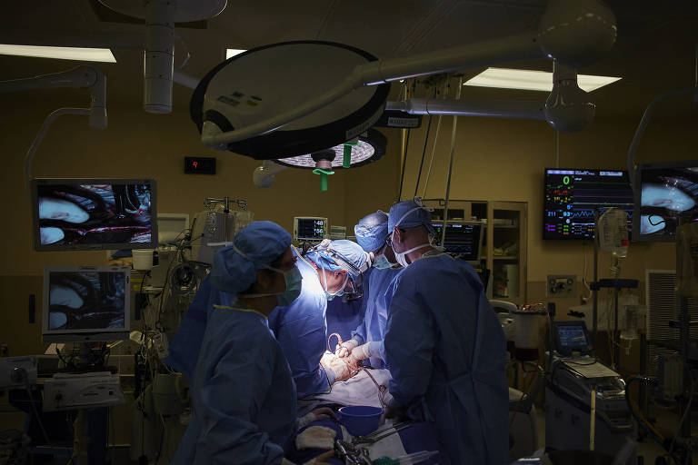Médicos, com as cabeças iluminadas pela luz de uma sala de cirurgia, fazem operação em paciente