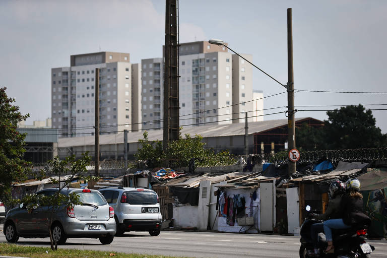 Contraste entre barracos da favela do Cimento e edifícios na zona leste de São Paulo; local exemplifica o problema da falta de moradia na capital paulista