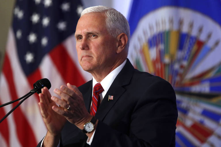De terno preto e gravata vermelha, Pence aplaude diante de um microfone; ao fundo, aparecem à esquerda uma bandeira dos EUA e à direita, o símbolo da OEA sob fundo azul