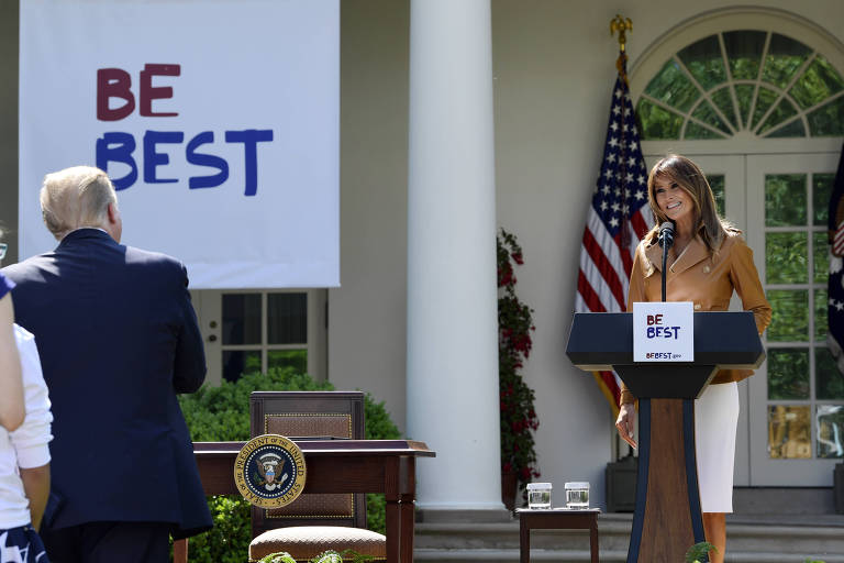 De camisa marrom e saia branca, Melania Trump aparece rindo em um púlpito com a mensagem "Be Best" (Seja melhor, em inglês) em frente a uma das entradas da Casa Branca. O símbolo, em fundo branco com "be" escrito em vermelho e "best" em azul, reaparece em um cartaz à esquerda da imagem. Também à esquerda, Donald Trump aparece de costas aplaudindo a mulher. Ao lado direito dele, está uma mesa com o escudo presidencial americano e atrás de Melania, uma das portas da Casa Branca com as bandeiras americana e da Presidência.