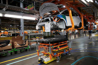 An automated guided vehicle carrying a battery pack moves under a partially assembled 2018 Chevrolet Bolt EV vehicle on the assembly line at General Motors Orion Assembly in Lake Orion,