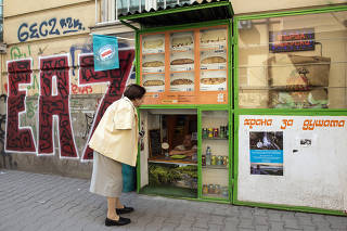 A customer speaks with a vendor selling food and snacks, at knee-level in the service window of a klek, or squat shop, in Sofia, Bulgaria.