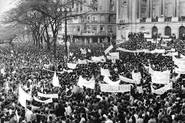 Multidão carregando faixas, em foto em preto e branco 