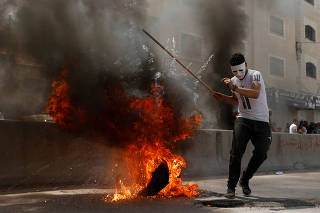 Palestinian demonstrator reacts next to a burning tire during a protest against U.S. embassy move to Jerusalem and ahead of the 70th anniversary of Nakba, near Israeli Qalandia checkpoint near Ramallah in the occupied West Bank