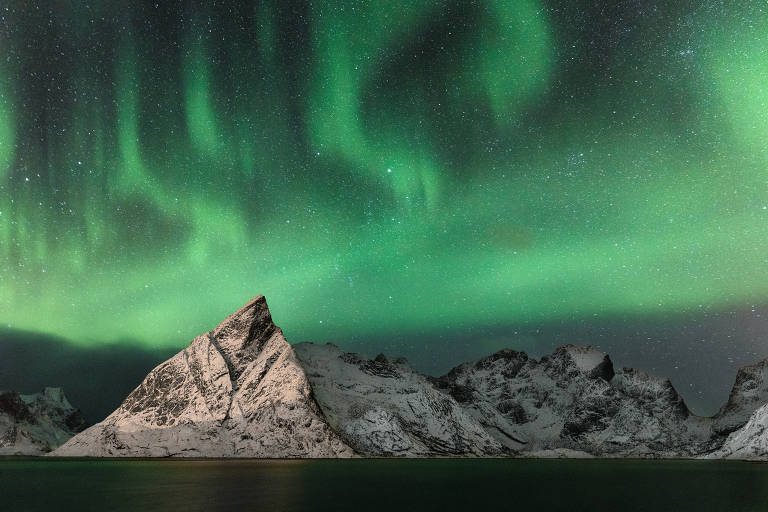 Aurora boreal fotografada acima de montanhas com neve na Noruega