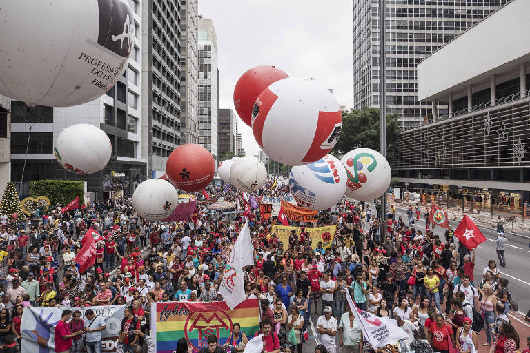 Pessoas vestidas de vermelho carregam cartazes e balões na avenida paulista, em São Paulo