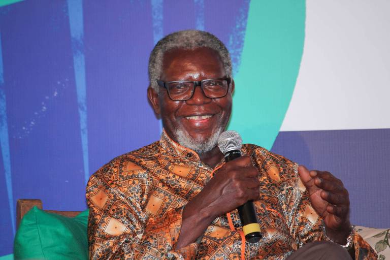 Retrato do antropólogo Kabengele Munanga, sentado, com um microfone na mão