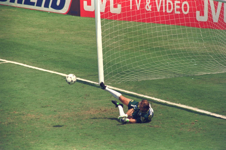 A imagem mostra Taffarel caído no chão, à frente do gol, após defender a bola