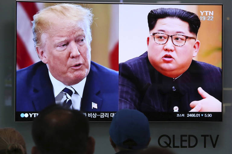 Fotos de Trump e Kim aparecem em TV, abaixo da qual aparece a inscrição QLED TV. À frente, um grupo de três pessoas, cujas cabeças aparecem. Uma delas, ao centro, está de gorro azul.