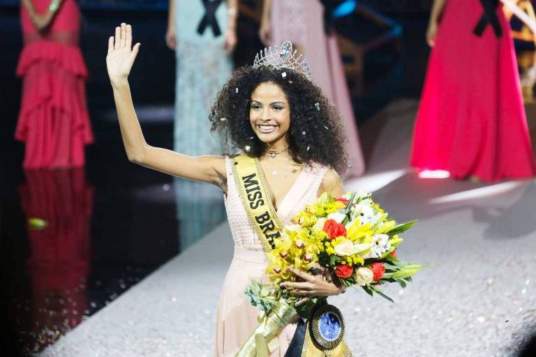 Monalysa Alcântara, vencedora do concurso Miss Brasil 2017, acena para plateia com flores na mão, faixa e coroa na cabeça