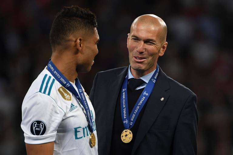 Homem com terno e medalha conversa com homem de camiseta branca e medalha 