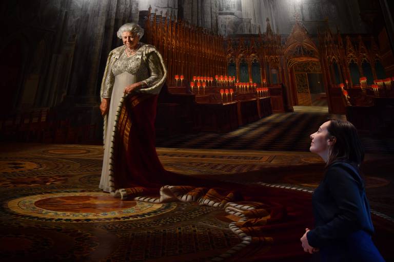 Uma mulher posa ao lado de quadro que mostra um retrato da rainha Elizabeth 2ª