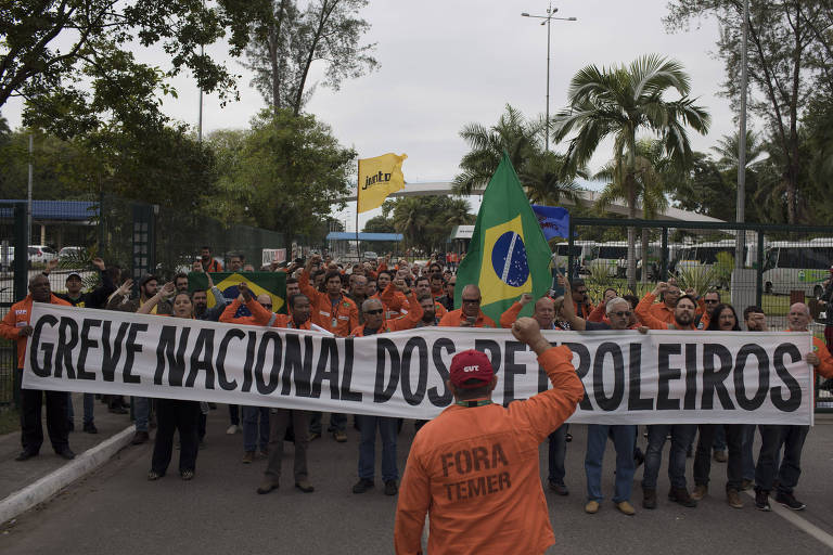 Petroleiros de uniforme laranja andam em fila segurando faixa que diz "greve nacional dos petroleiros"