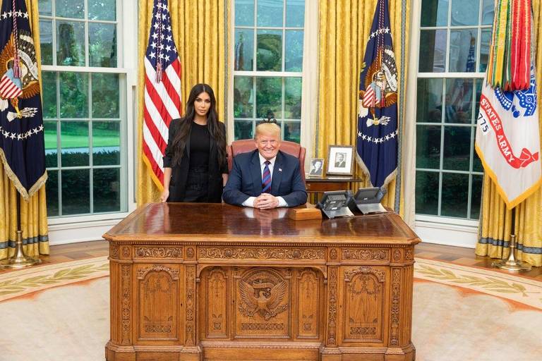 kim kardashian em pé ao lado de trump sentado em sua mesa 