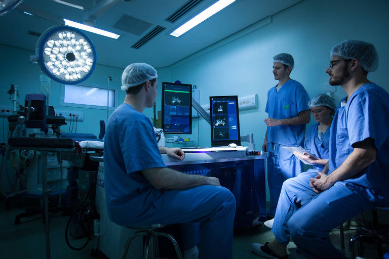 Médicos em sala de cirurgia analisam imagem em tela de computador