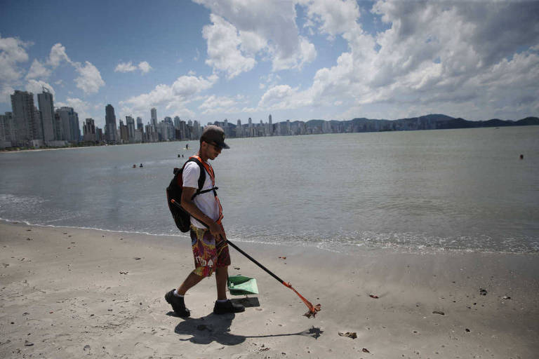 Funcionário retira sujeira de areia da praia em Balneário Camboriú (SC)