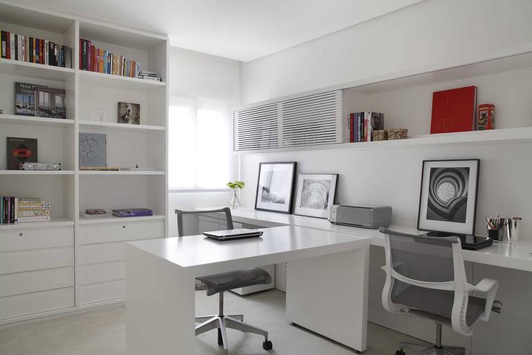 Escritório com estantes, mesa e paredes brancas, cadeiras cinzas e objetos coloridos