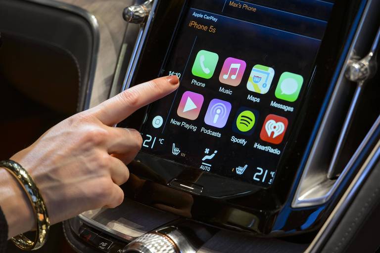 Uma mão aponta para o painel digital de um carro, com tela touchscreen