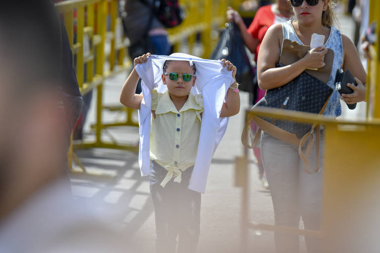 Menino cobre a cabeça para se proteger do sol enquanto cruza a ponte Simón Bolivar 
