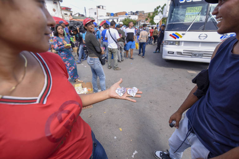 Jovens fazem origami na aglomeração que se forma antes da fronteira que leva à Colômbia
