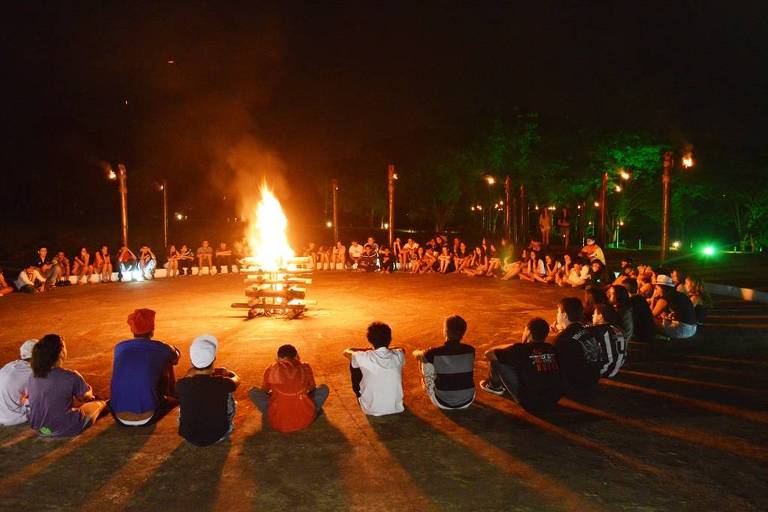 Pessoas sentadas no chão, em roda, com fogueira no centro