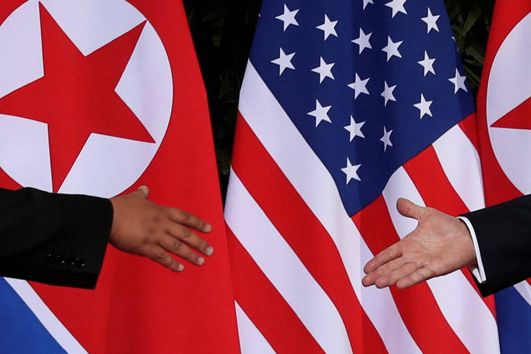 A mão de Kim Jong-un aparece à esquerda, com um pedaço de sua camisa preta. Do lado direito está a de Donald Trump e pode-se ver uma parte de seu paletó preto e da camisa branca que usa por baixo. Ao fundo, estão as bandeiras da Coreia do Norte e dos Estados Unidos.