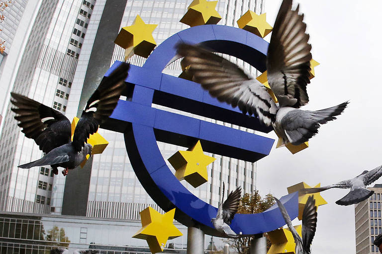 Pombos voam perto de escultura com símbolo do euro do prédio do BCE, em Frankfurt, na Alemanha