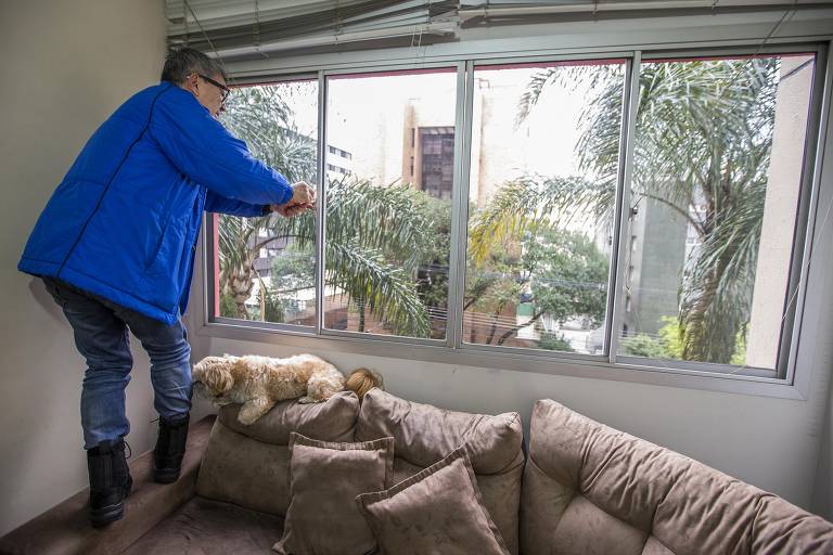 Ishii sobe no sofá para abrir as persianas das janelas de seu apartamento de 70 m², em Curitiba 