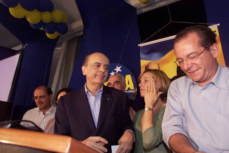 O candidato do PSDB, José Serra, durante pronunciamento em que admitiu a derrota para o candidato Luiz Inácio Lula da Silva, em 2002; a seu lado, a candidata a vice, Rita Camata, que chorou durante o discurso, e o presidente nacional do PSDB, José Aníbal