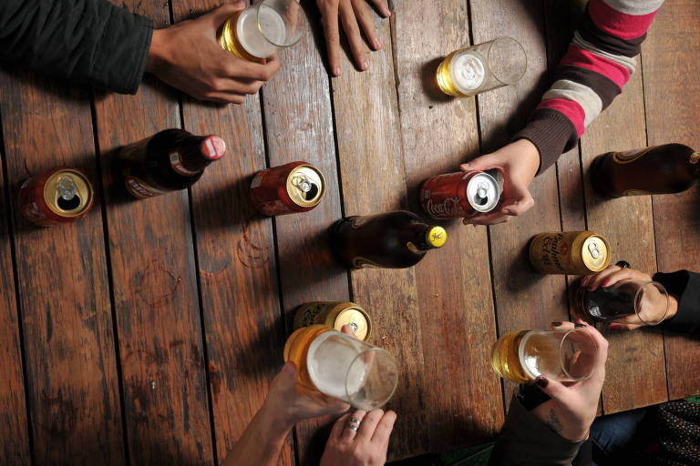 Pessoas bebendo, com copos, latinhas e garrafas sobre a mesa