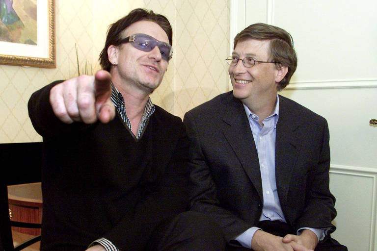 Bono Vox aponta para a câmera, ao lado de Bill Gates