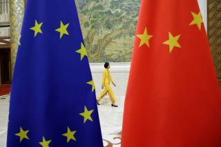 An attendant walks past flags of EU and China ahead of the EU-China High-level Economic Dialogue in Beijing