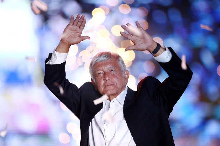 López Obrador usa blazer preto e camisa branca. Ele levanta os dois braços para o alto. Ao fundo, aparecem esmaecidos papéis picados e fogos de artifício.