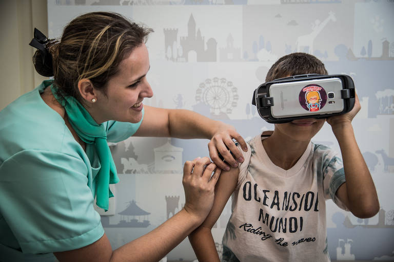 Com o auxílio de realidade virtual, uma clínica de Barueri busca distrair as crianças na hora da vacinação. Na foto, a enfermeira Mayra Ardito, 30, aplica a vacina de meningite B em Enzo Fraga, 9